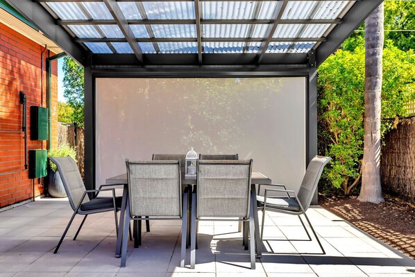 A covered patio with a table and chairs, a brick wall, and a metal roof.