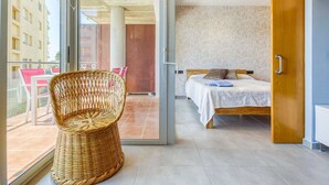 Een moderne hotelkamer met een bed, een rieten stoel en uitzicht op de stad door grote ramen.