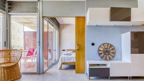 Een moderne woonkamer met een bed, een grote wandklok en een schuifdeur die leidt naar een terras.