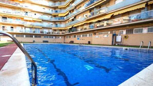 A swimming pool with a clear blue water surface, surrounded by a multi-story building with balconies. - Lovely apartment for 4 people with WIFI, pool, A/C, TV and balcony (Santa Susanna)