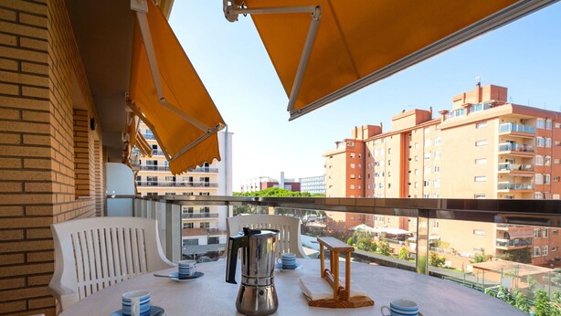 A balcony with a table set for four, a coffee pot, and a view of surrounding buildings. - Lovely apartment for 4 people with WIFI, pool, A/C, TV and balcony (Santa Susanna)