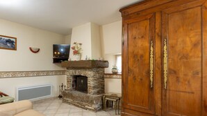 Ein Wohnzimmer mit Kamin aus Stein, einem Holzschrank, einem Fernseher und einem Sofa.