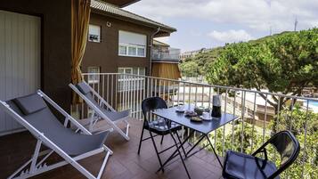 Un balcón con dos sillones de descanso, una mesa y sillas, y vistas a una piscina y zonas verdes.