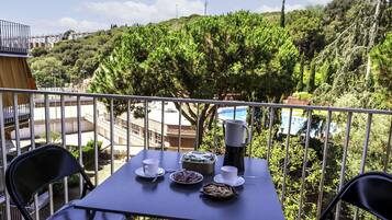 Un balcón con una mesa lista para dos personas, con vista a una piscina y abundante vegetación.