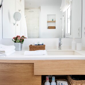 Ein modernes Badezimmer mit einem weißen Waschbecken, einem Spiegel, einer Dusche und einer kleinen Ablage mit Toilettenartikeln.