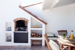 Eine Terrasse im Freien mit einem gemauerten Pizzaofen, einem Holztisch mit einem Stuhl und einem Regal mit Feuerholz und Zitronen.