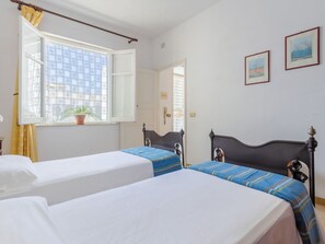 A room with two beds, a window with curtains, a potted plant, and two framed pictures on the wall. - Lovely apartment for 5 guests with WIFI, A/C, TV and terrace (San Vito Lo Capo)