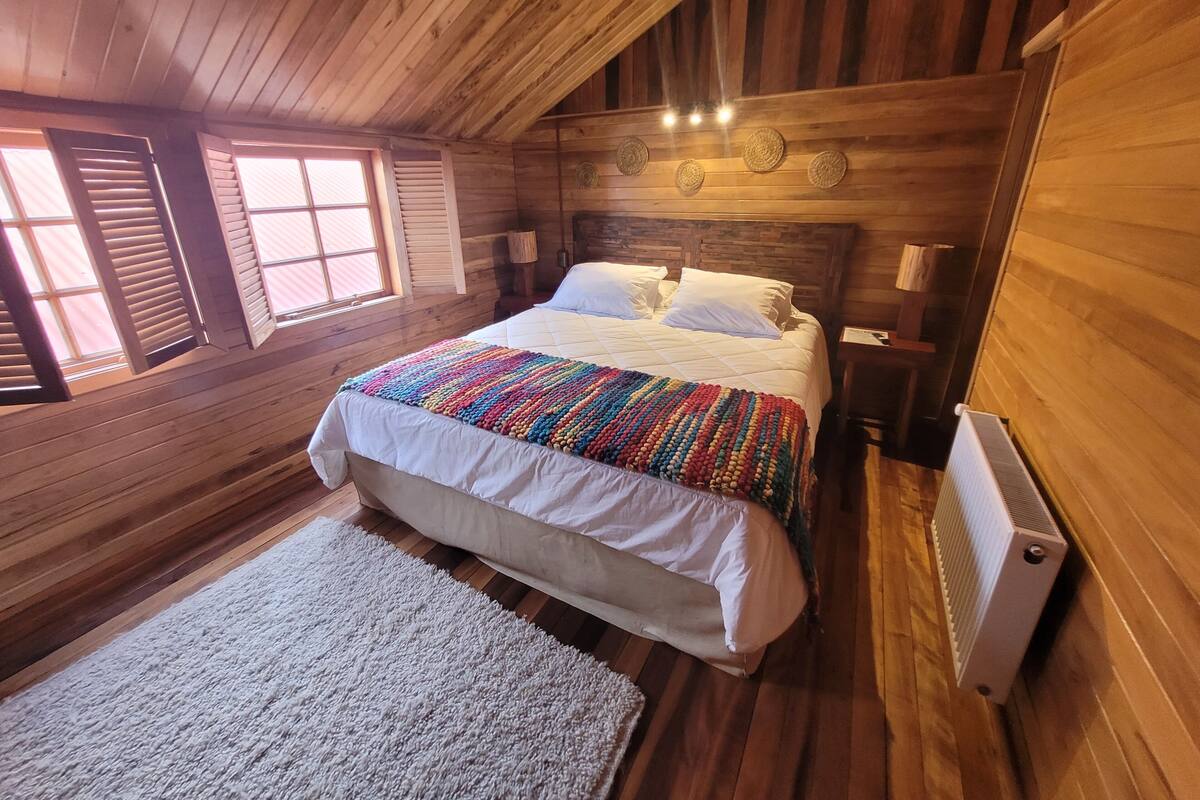 A cozy wooden cabin bedroom with a large bed, a white rug, and a radiator.