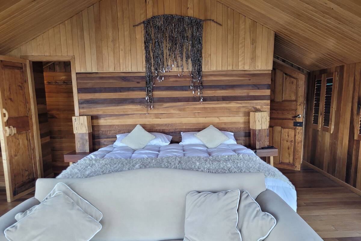 A cozy bedroom with a wooden ceiling, a large bed with white bedding, and a sofa with matching cushions.
