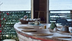 Een rustieke houten tafel met een witgeschuurde afwerking, geplaatst op een houten terras met kleurrijke kussens.
