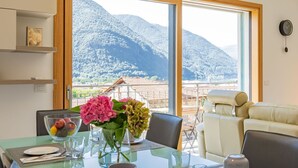 Un comedor con una mesa dispuesta para dos, un florero con flores y vistas a montañas a través de amplios ventanales.