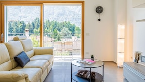 Una sala moderna con un sofá, una mesa de centro redonda de vidrio, un reloj y vistas a un paisaje nevado a través de amplios ventanales.