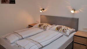 Un dormitorio con cama, dos mesitas de noche, cabecera y luces fijadas a la pared.