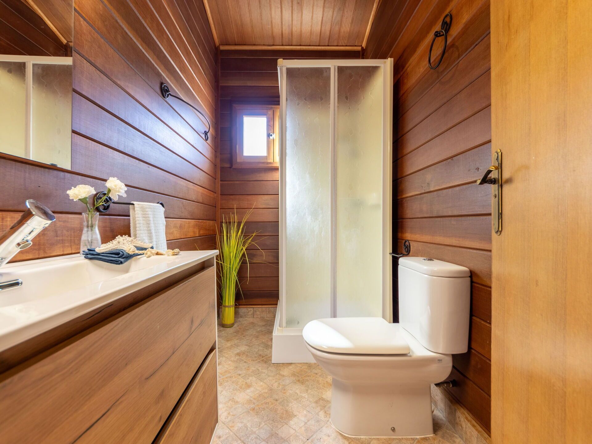 Un baño pequeño con paredes de madera, un lavabo blanco, un inodoro y una cabina de ducha.