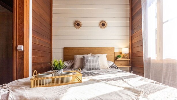 Ein gemütliches Schlafzimmer mit einem Holz-Kopfteil, einem Bett mit gemusterten Betttextilien, einem Nachttisch mit Lampe und einer kleinen Pflanze.
