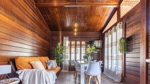 Ein gemütliches Zimmer mit Holzwänden und -decke, einer Couch mit Kissen, einem Esstisch mit Stühlen und Topfpflanzen.