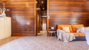 Ein gemütliches Zimmer mit Holzwänden, einer Couch mit Kissen, einem kleinen Tisch mit Lampe und einem Schrank.