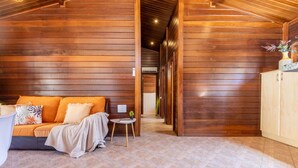 Ein gemütliches Zimmer mit Holzwänden, einem Sofa, einem kleinen Tisch mit Lampe und einem Schrank.