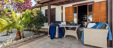 Eine überdachte Terrasse mit Korbmöbeln, einem kleinen Tisch und einer Sitzecke.