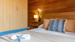 Ett hotellrum med en sänggavel i trä, en säng med mönstrade kuddar, ett nattduksbord med en lampa och en vas med blommor samt en sjöstjärnedekoration på sängen.