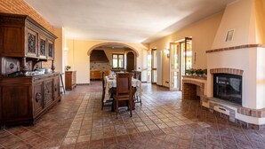 A spacious kitchen with a dining area, featuring a fireplace, wooden cabinets, and a tiled floor.