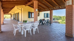 An outdoor covered patio with brick flooring, white plastic chairs, and a table with flowers.
