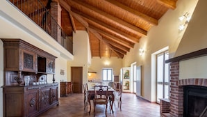 A spacious dining area with a wooden table and chairs, a fireplace, and a high ceiling with exposed beams.