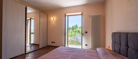 A bedroom with a large bed, a sliding door, a radiator, and a view of greenery outside.