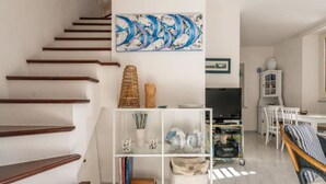 Un escalier mène à un espace de vie comprenant une bibliothèque blanche, un téléviseur et un coin repas avec un buffet blanc et des chaises.