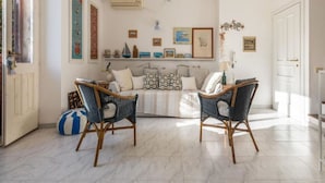 Un salon comprenant un canapé, deux fauteuils en osier, un tapis à motifs et des éléments de décoration murale.