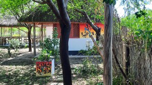 A covered outdoor area with a wooden deck, a thatched-roof structure, and a mural on a building wall. - Real African Life Safaris and Camps (Bariadi)