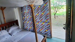 A bedroom with a wooden bed, white bedding, a canopy, and a colorful patterned curtain. - Real African Life Safaris and Camps (Bariadi)