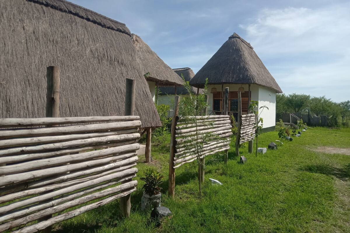 Fachwerkhäuser mit Strohdächern und Holzzaunen, umgeben von viel Grün.