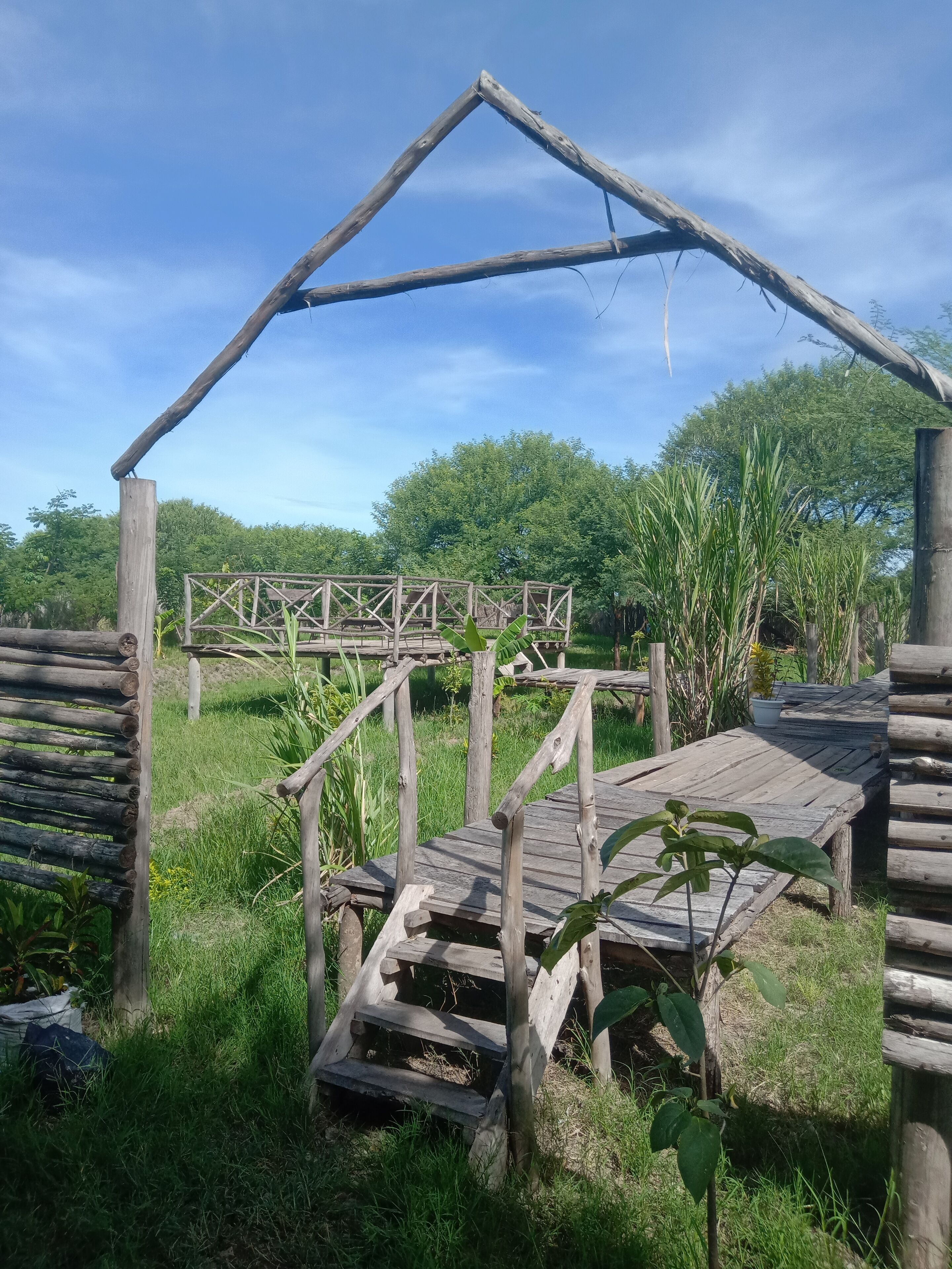 A rustic wooden structure with a triangular roof, surrounded by lush greenery and trees.