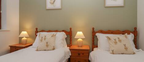 A double room with two beds, each with a wooden headboard, white bedding, and a pillow with a rabbit print. There are two bedside tables with lamps, and the walls are painted a light green.