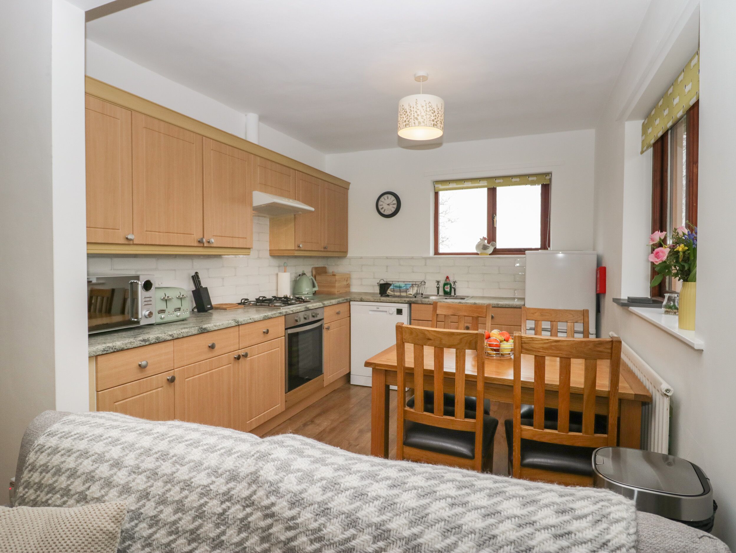 A compact kitchen with wooden cabinets, a dining table with chairs, a built-in oven, and a small window with a view.