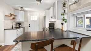 Une cuisine moderne avec des meubles blancs, un îlot central en marbre foncé et des chaises en bois.