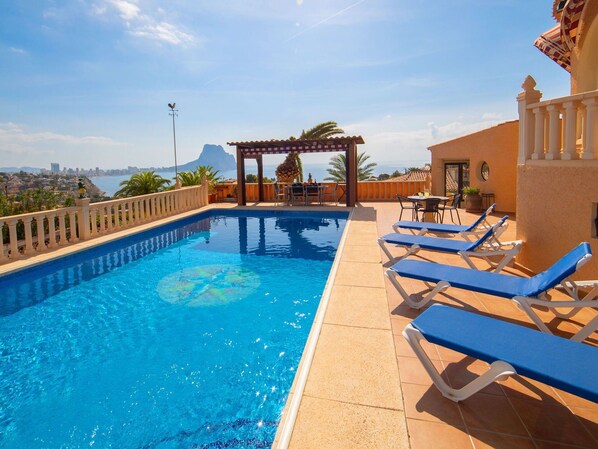 Ein Swimmingpool mit blauem Wasser, umgeben von Liegestühlen und einer Pergola.