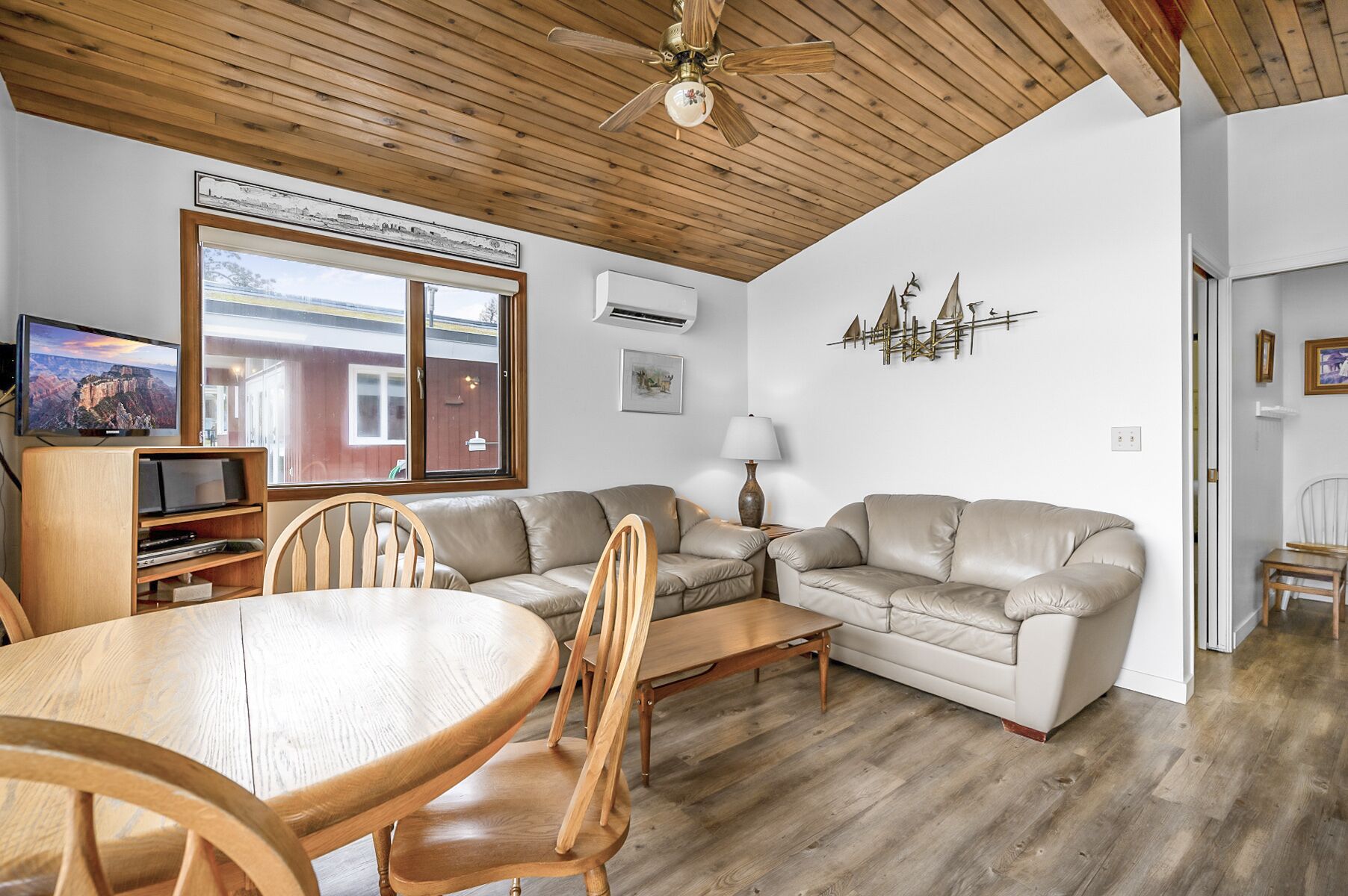 A living room with a wooden ceiling, a television, a sofa, a coffee table, and a dining table with chairs.