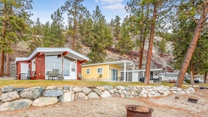 A cabin with a stone wall, a fire pit, and a covered outdoor seating area.