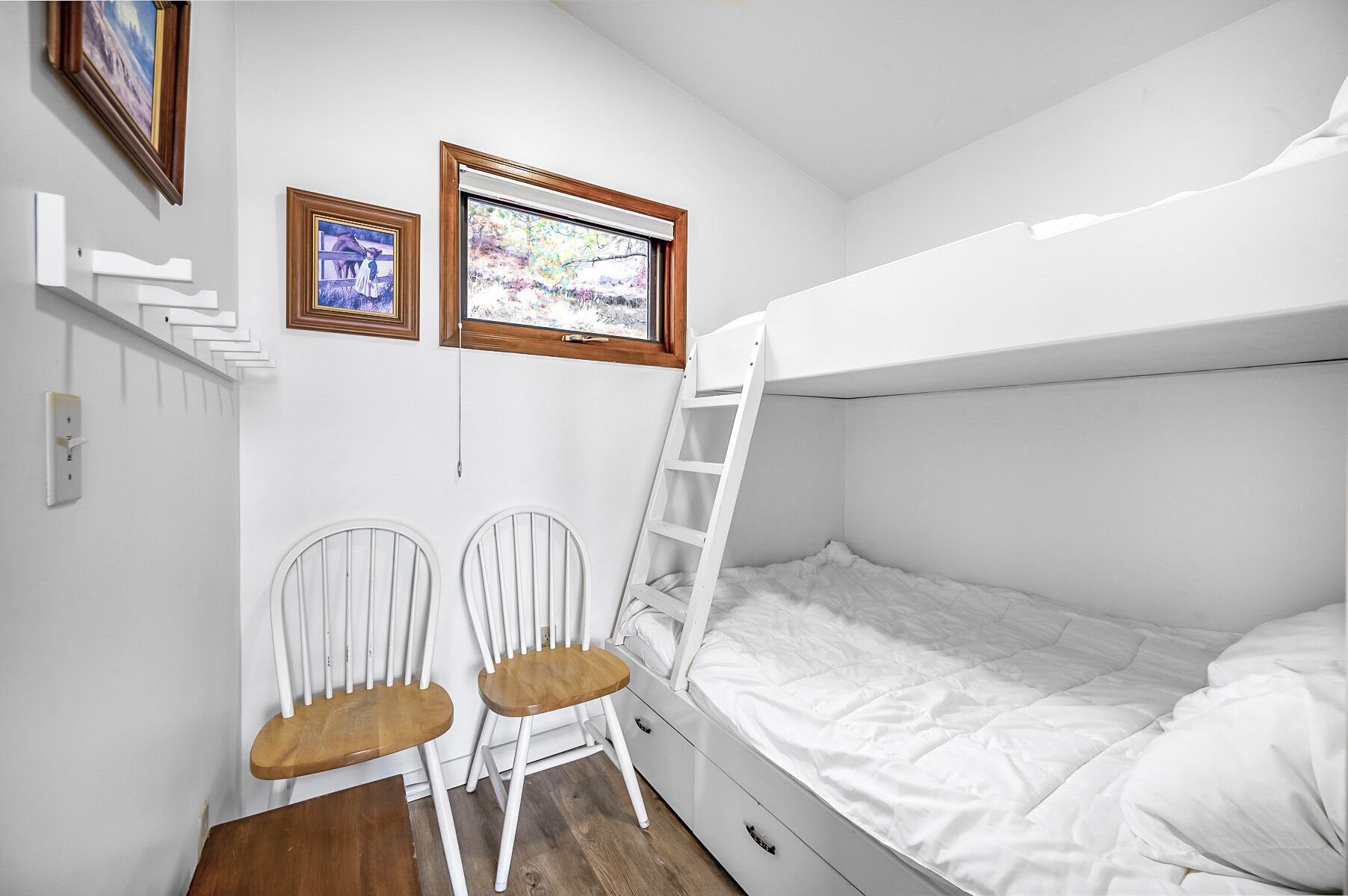 A bunk bed room with two white chairs, a ladder, and two framed pictures on the wall.