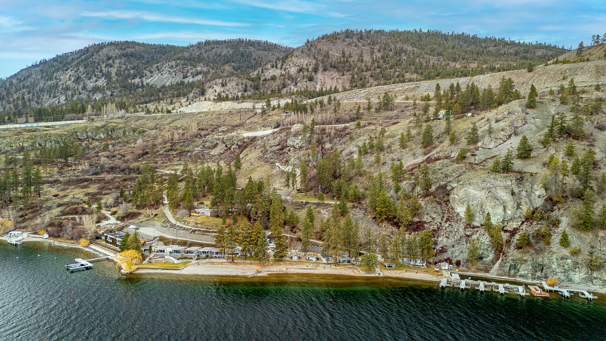 A lakeside property with a dock, a small building, and a road leading up the hill.