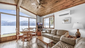 A spacious living room with a large window overlooking a lake, a ceiling fan, and a fireplace.