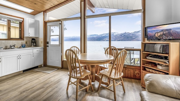A modern kitchen with a view of a lake and mountains, wooden furniture, and a television.