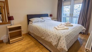 Une chambre bien rangée, avec un lit, des tables de chevet, un miroir et une fenêtre avec des rideaux.