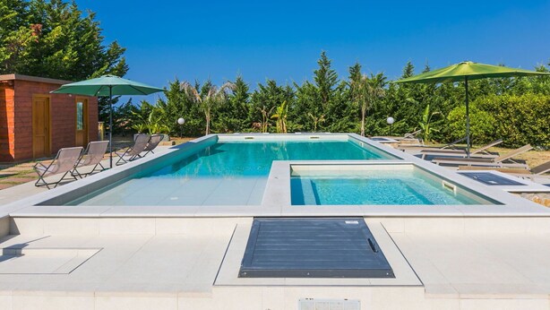 Ein rechteckiger Pool mit zwei Bereichen, umgeben von Liegestühlen und Sonnenschirmen.