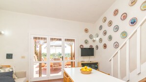 Un salon lumineux avec un canapé blanc, une table à manger avec des chaises, un téléviseur et un escalier.