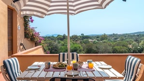 Une terrasse avec une table dressée pour le petit-déjeuner, des chaises à rayures et un parasol à rayures.