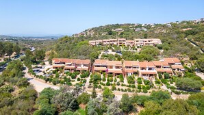 Un quartier résidentiel situé sur une colline, avec des maisons à étages, un ciel dégag é et une vue lointaine sur la mer.