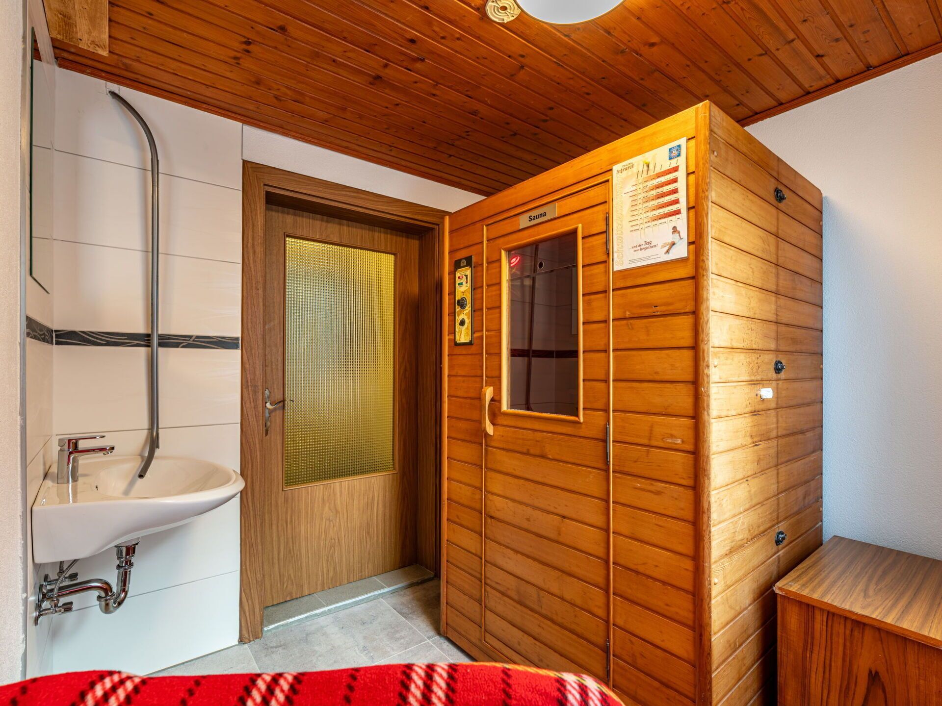 Een sauna met een houten deur, een raam en een poster aan de muur.